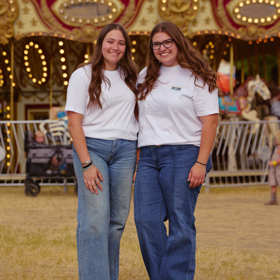Two young women smiling in front of a carousel on the midway at the Wyoming State Fair.
