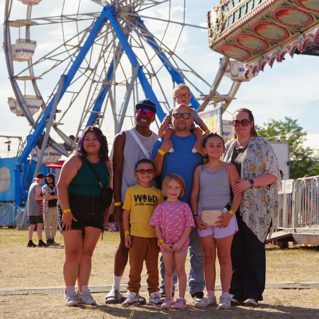 Family posing together in front of a Ferris wheel on the midway at the Wyoming State Fair.