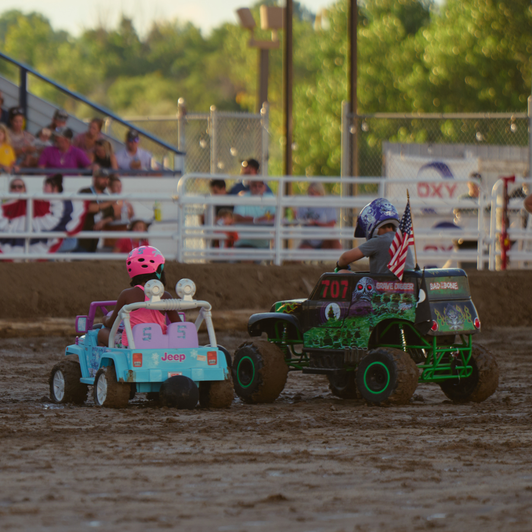 Children drive small toy vehicles in the Ford Grandstand Arena during a Power Wheels derby event at the Wyoming State Fair as spectators watch from the grandstands.